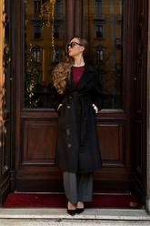 a lady in a red top, a long black wool coat and a pair of grey pants